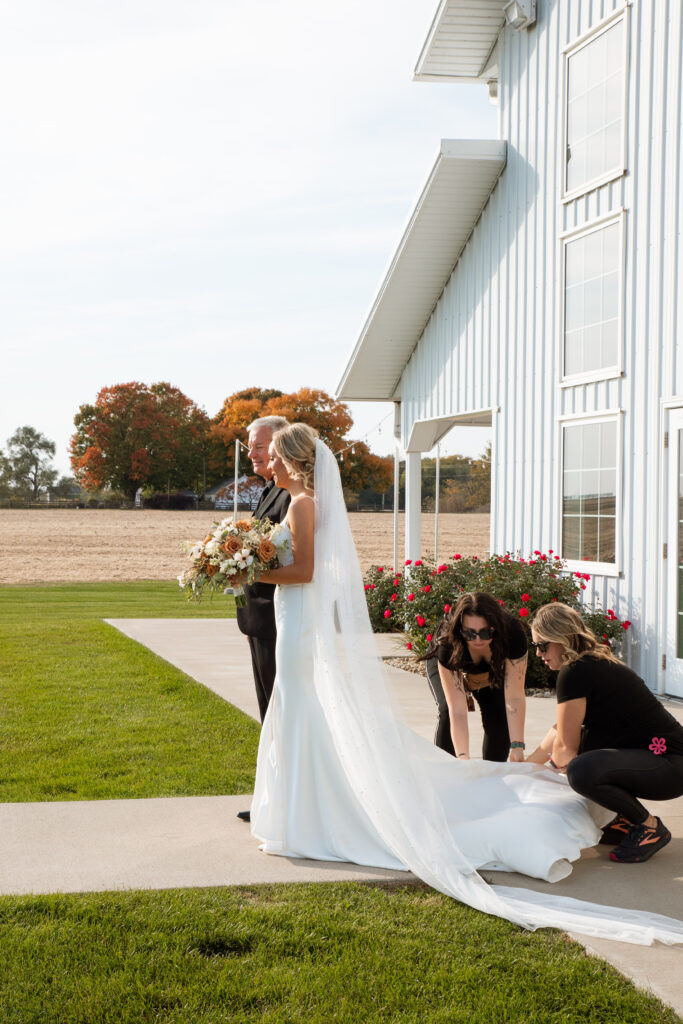 bride getting ready to walk down the aisle as staff fluff her dress